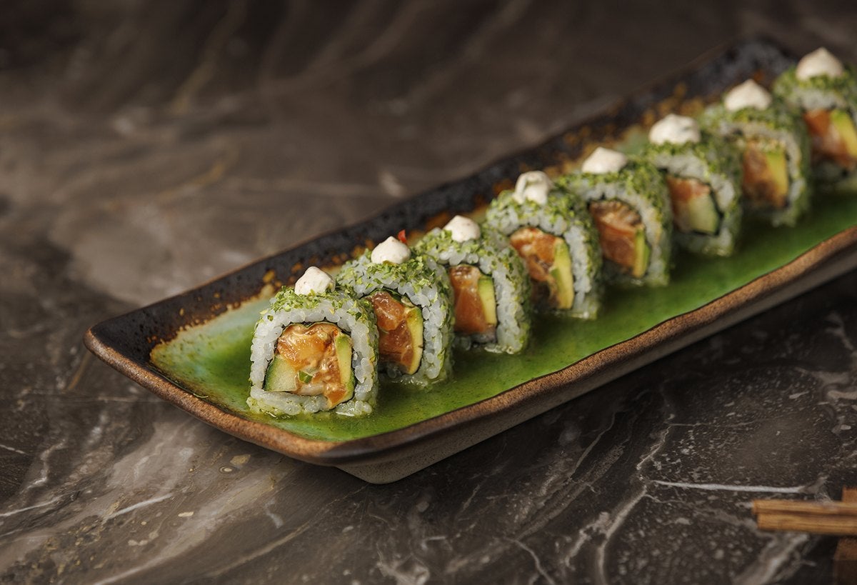 A rectangular green sushi plate of Mr. H's Jade Roll: bites of spicy salmon, avocado, cucumber, jalapeño ponzu, wasabi crema, and basil in rice and nori.