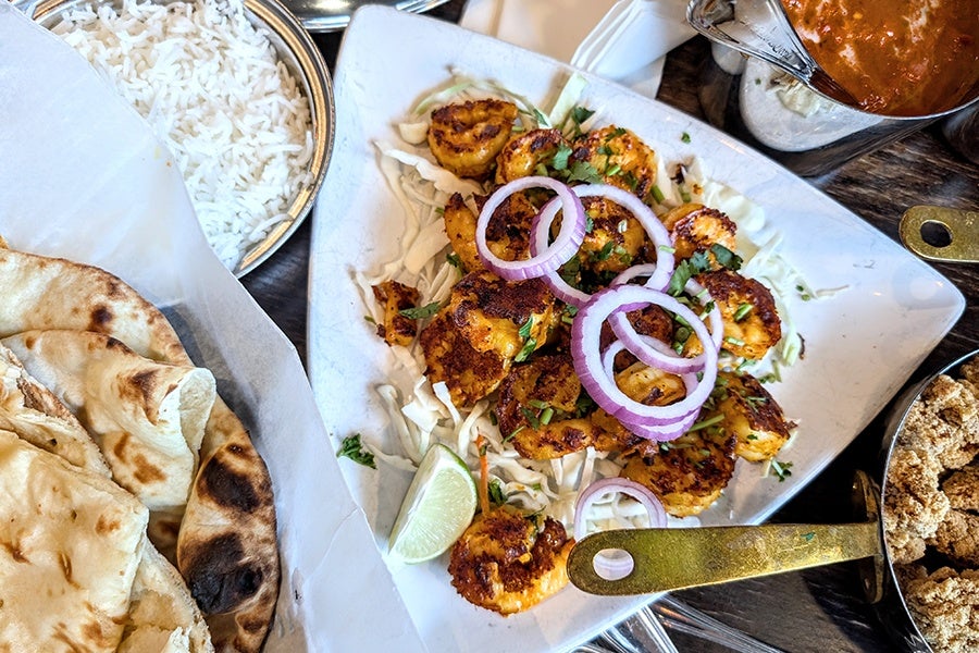 Overhead view of Indian dishes, including grilled shrimp topped with rings of raw red onion, white rice, and naan.