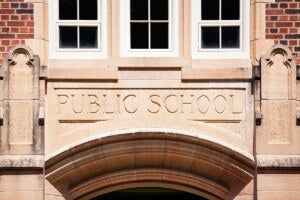 Stone archway above a doorway with the words "PUBLIC SCHOOL" carved into it, set in a brick building with three white-framed windows above.